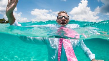 Over-under view of businessman holding his hand up to call for help trying to keep afloat in clear turquoise waters after a boat mishap in Washington state.