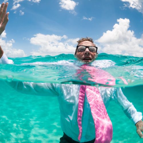 Over-under view of businessman holding his hand up to call for help trying to keep afloat in clear turquoise waters after a boat mishap in Washington state.