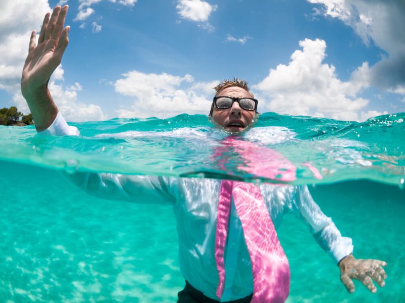Over-under view of businessman holding his hand up to call for help trying to keep afloat in clear turquoise waters after a boat mishap in Washington state.
