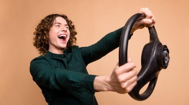 A young male driver holding a steering wheel and smiling because he has teen driver insurance WA
