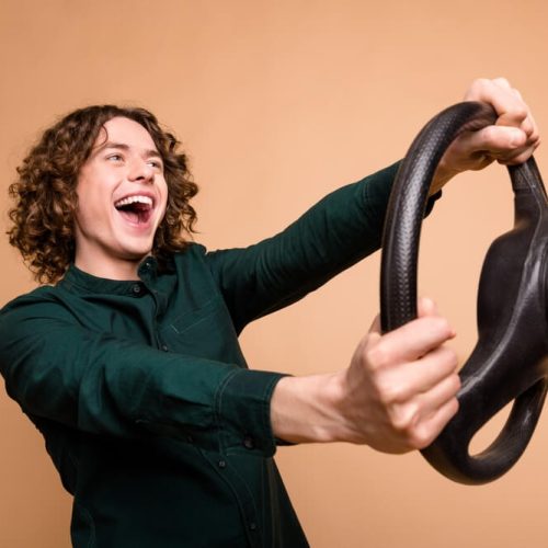 A young male driver holding a steering wheel and smiling because he has teen driver insurance WA