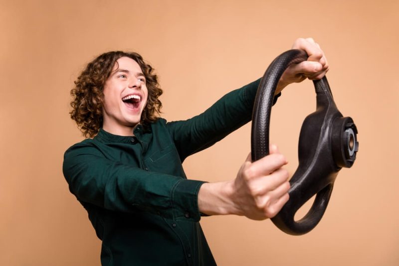 A young male driver holding a steering wheel and smiling because he has teen driver insurance WA