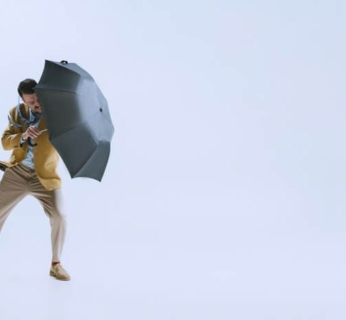Bad weather. Portrait of young businessman fighting the wind with umbrella isolated on white background. Concept of rain and how to protect your business with the right insurance in Washington.