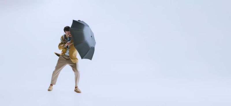 Bad weather. Portrait of young businessman fighting the wind with umbrella isolated on white background. Concept of rain and how to protect your business with the right insurance in Washington.