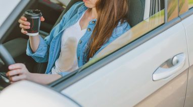 Female spilling coffee on herself while driving a car, how coffee can make you have an accident, having cheap car insurance in Washington State.
