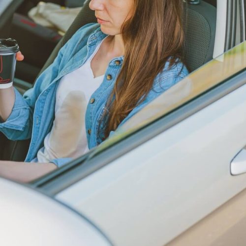 Female spilling coffee on herself while driving a car, how coffee can make you have an accident, having cheap car insurance in Washington State.