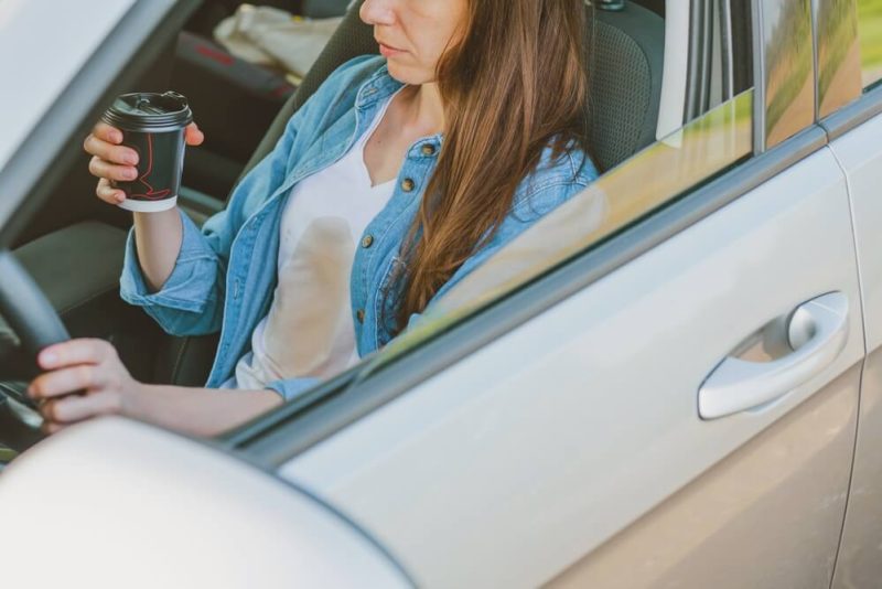 Female spilling coffee on herself while driving a car, how coffee can make you have an accident, having cheap car insurance in Washington State.