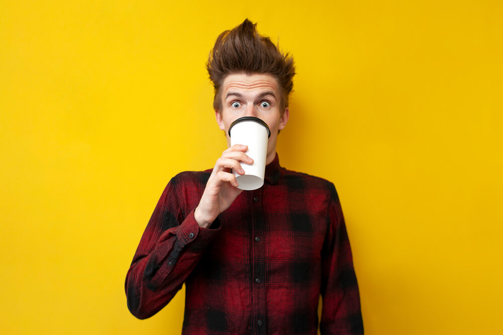 Young shocked guy drinks invigorating coffee and is caffeinated, driving safely with cheap car insurance in Seattle.