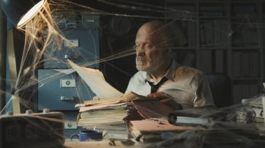 Man searches for his insurance policy in a dusty office with spider webs, concept of reviewing and updating insurance policy regularly.