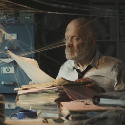 Man searches for his insurance policy in a dusty office with spider webs, concept of reviewing and updating insurance policy regularly.