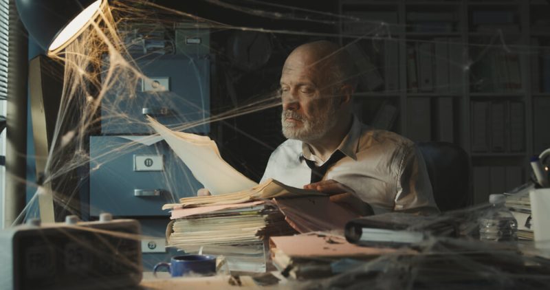 Man searches for his insurance policy in a dusty office with spider webs, concept of reviewing and updating insurance policy regularly.