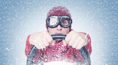 Vern-Fonk-when-your-car-turns-into-an-ice-cube-winter-auto-insurance-tips-in-washington-1  Man wearing a winter jacket and snow goggles holding a steering wheel, illustrating winter auto insurance tips for safe driving in snowy conditions.