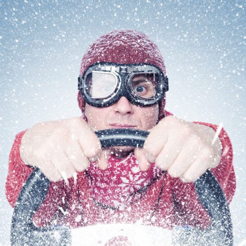 Man wearing a winter jacket and snow goggles holding a steering wheel, illustrating winter auto insurance tips for safe driving in snowy conditions.