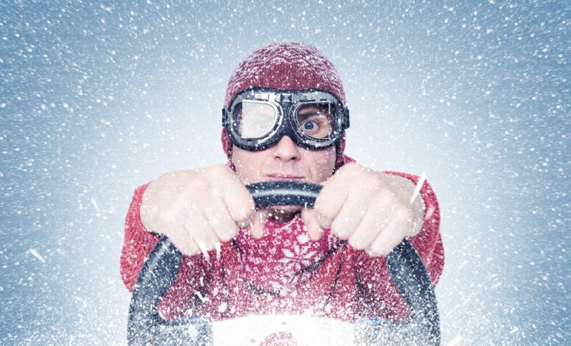 Vern-Fonk-when-your-car-turns-into-an-ice-cube-winter-auto-insurance-tips-in-washington-1  Man wearing a winter jacket and snow goggles holding a steering wheel, illustrating winter auto insurance tips for safe driving in snowy conditions.