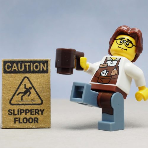 Mini toy of barista man serving in a cafeteria, holding a cup of coffee, about to slip on a wet floor next to a wet floor sign, highlighting business insurance in Washington.