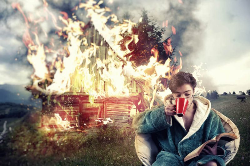 Man drinks coffee and reads a book while his house burns in the background, symbolizing insurance mistakes Washington.