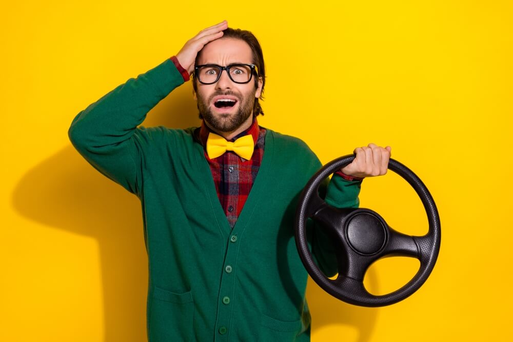Young man with brunet hair wearing a green jumper, panicking and holding his forehead while steering during a car incident, illustrating insurance mistakes Washington.