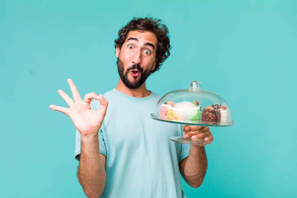 Funny picture of a guy holding up cake with the okay hand sign. He's happy because he's learning how to get the best car insurance.