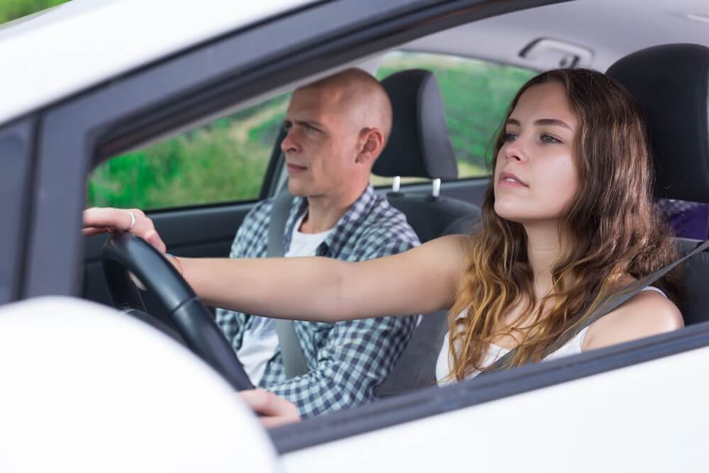 A young driver practices behind the wheel with an instructor in the passenger seat, representing situations where a student driver sticker Washington may be used.