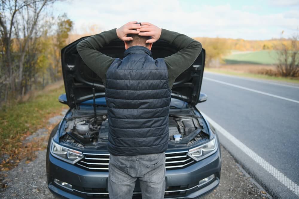 Driver standing by a broken-down car on the roadside, helping explain what does full coverage mean for unexpected vehicle issues.