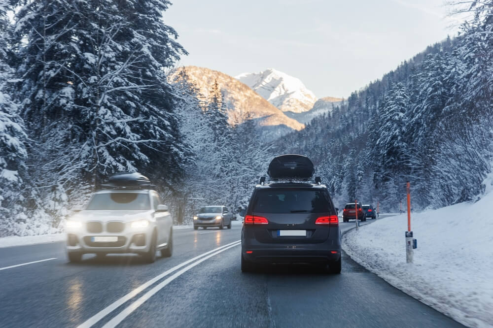 SUVs driving on a snowy mountain highway, including one with a rooftop cargo box, illustrating does auto insurance cover bike racks, cargo boxes, and rooftop gear.