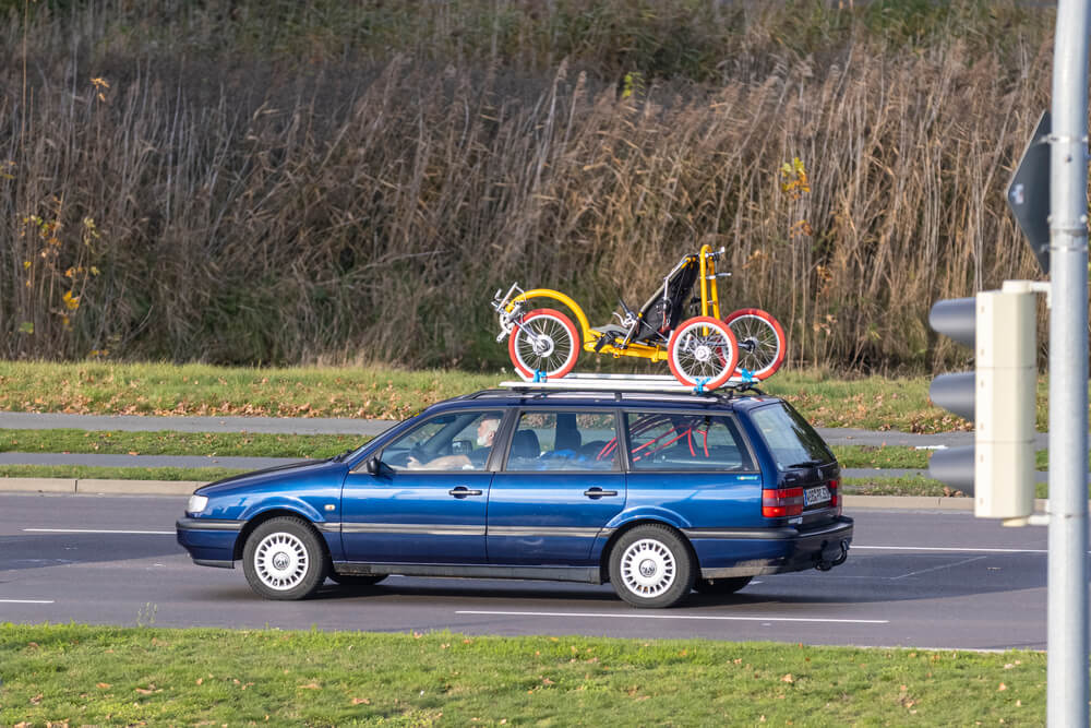 Blue station wagon driving on a road with bicycles secured on a rooftop rack, illustrating does auto insurance cover bike racks, cargo boxes, and rooftop gear.