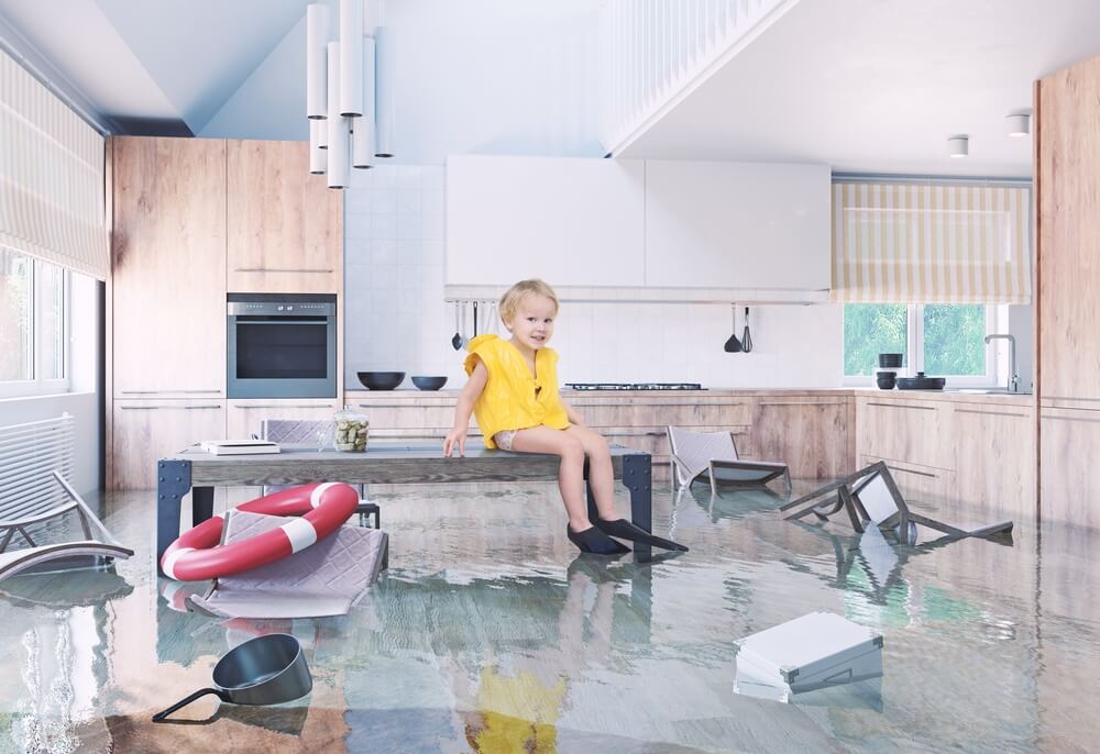 Child sitting on a kitchen island in a modern home with severe flooding and floating furniture, highlighting what your insurance needs look like after a major home upgrade.