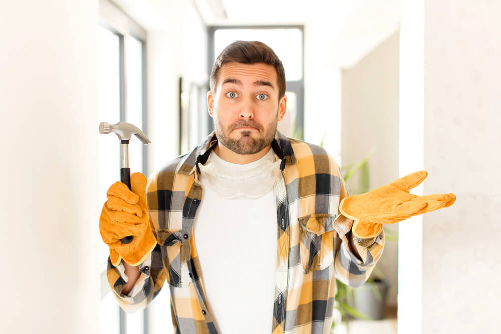 Homeowner in work gloves shrugs while holding a hammer inside a renovated house, showing what your insurance needs look like after a major home upgrade.