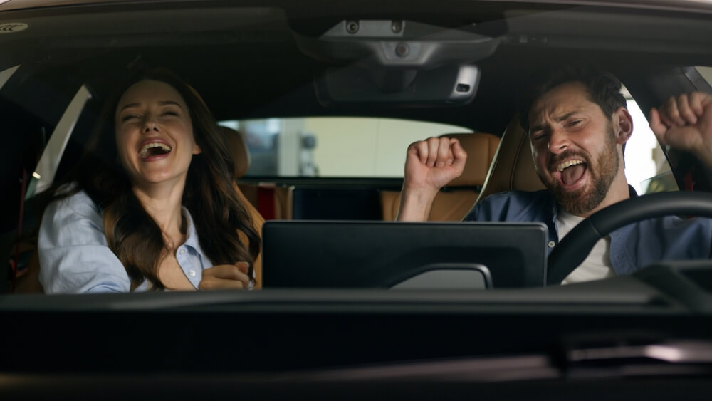 Two people laugh and enjoy the digital dashboard inside a modern car, showing how car technology can make the ride feel more interactive.