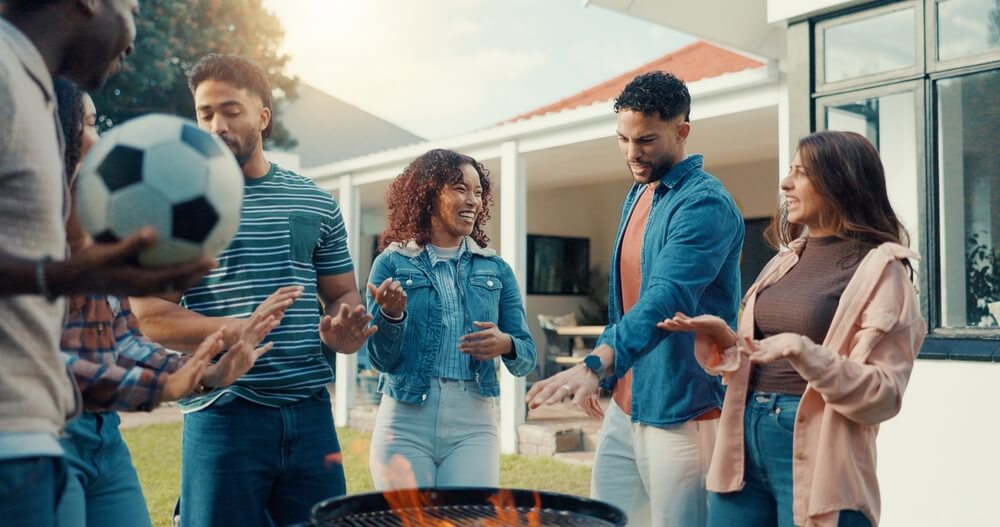Friends gather around a backyard fire pit near a home, showing why outdoor living spaces need more protection.