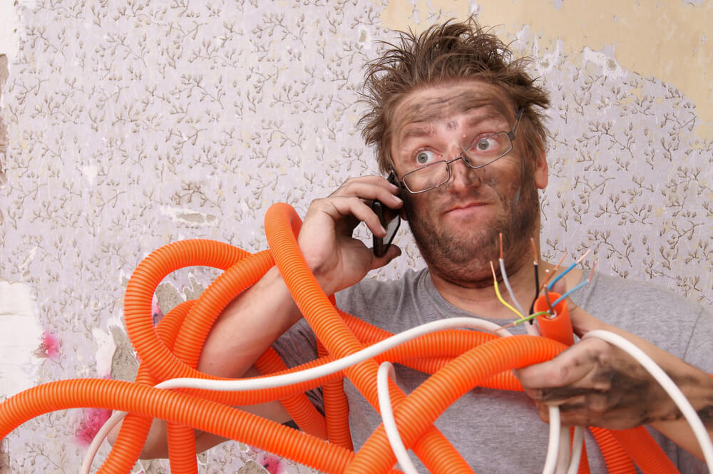 White man with spiky hair after trying to fix an electrical issue, holding electrical wires and on the phone about his business insurance in Washington.